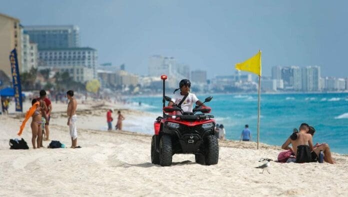 A lifeguard on an ATV monitoring a beach with people and ocean in the background.