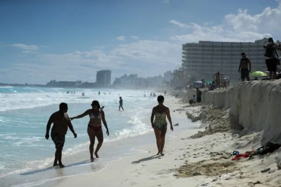 People enjoying a sunny day on a sandy beach in Cancun with waves and hotels in the background